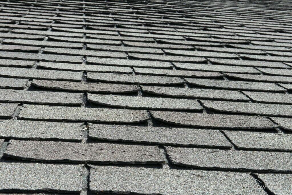 Asphalt shingles with edges curled and lifted away from the roof plane, giving the surface a wavy appearance.