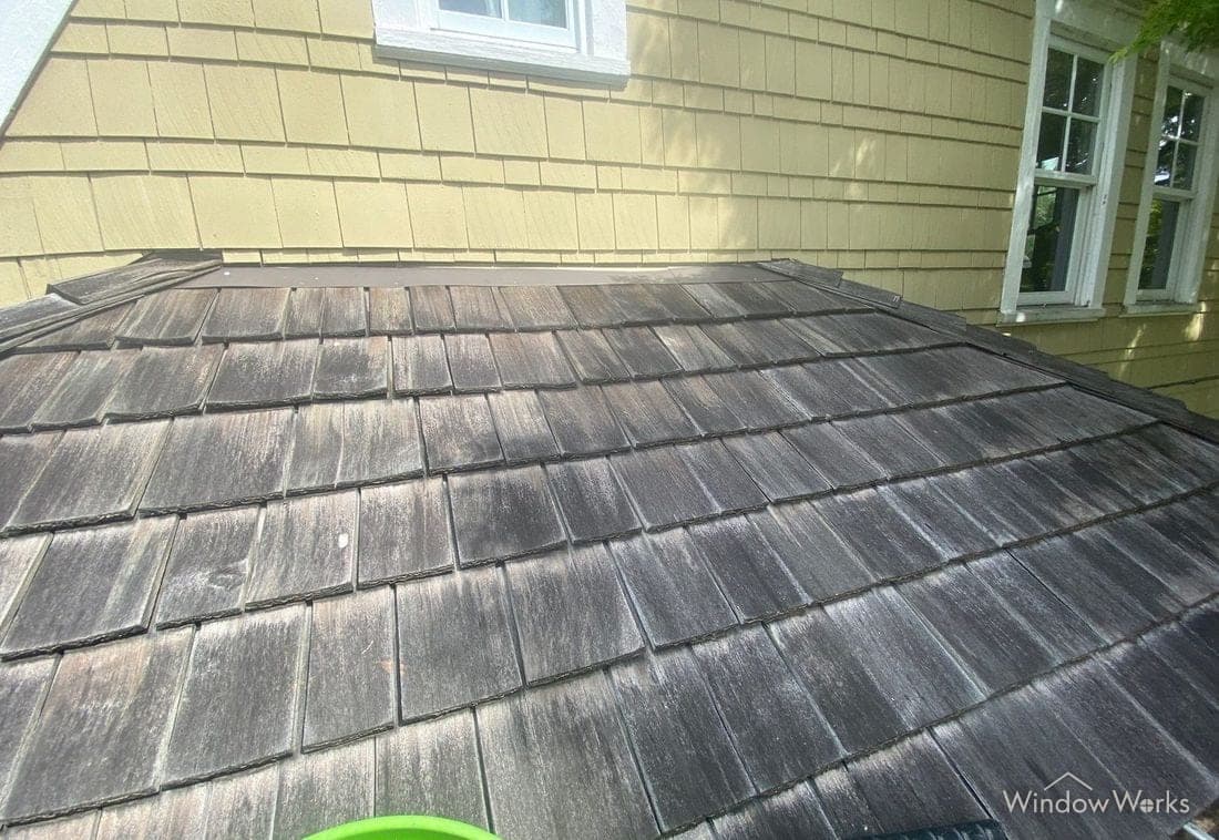 A cedar shake roof with an uneven gray-black cast from mold and algae covering the whole surface.