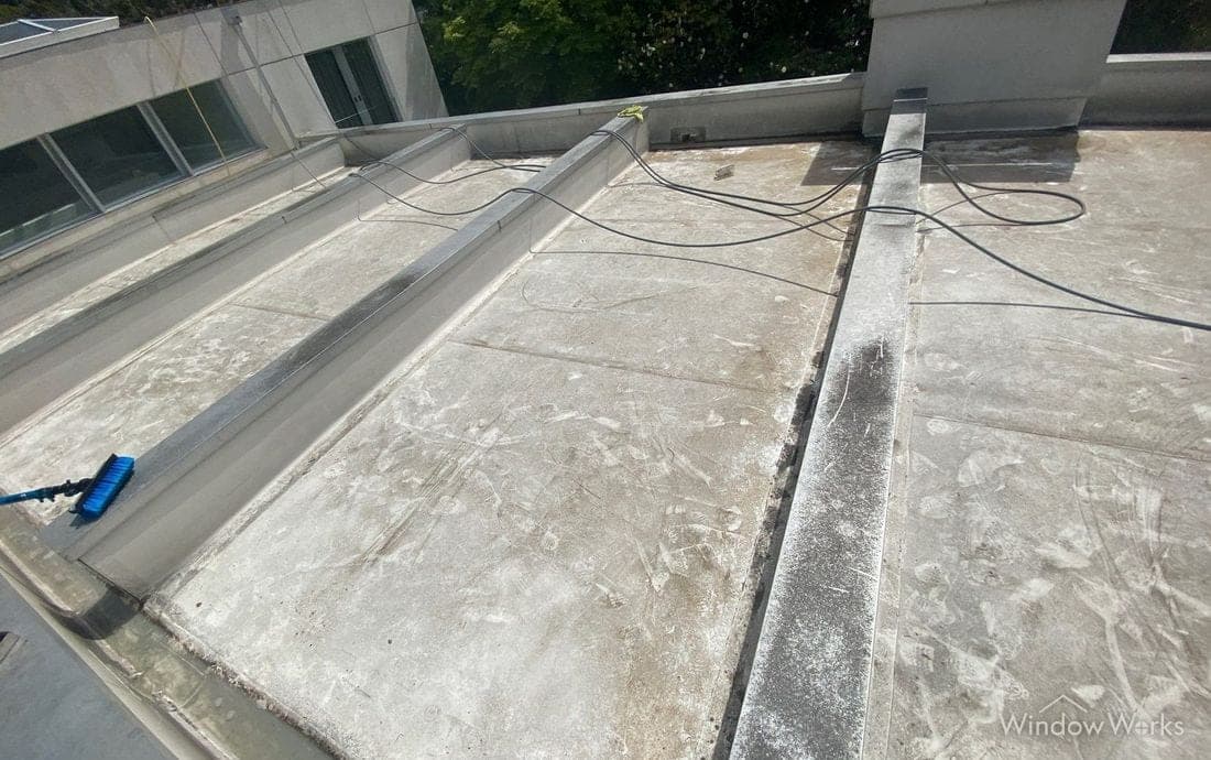 Dark algae growth running along the drainage troughs of a flat membrane roof beside a raised curb.