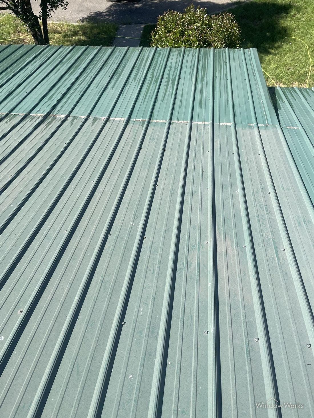 A green metal roof mid-restoration, with pale chalky oxidized panels beside deeply saturated panels that have had the oxidation removed.