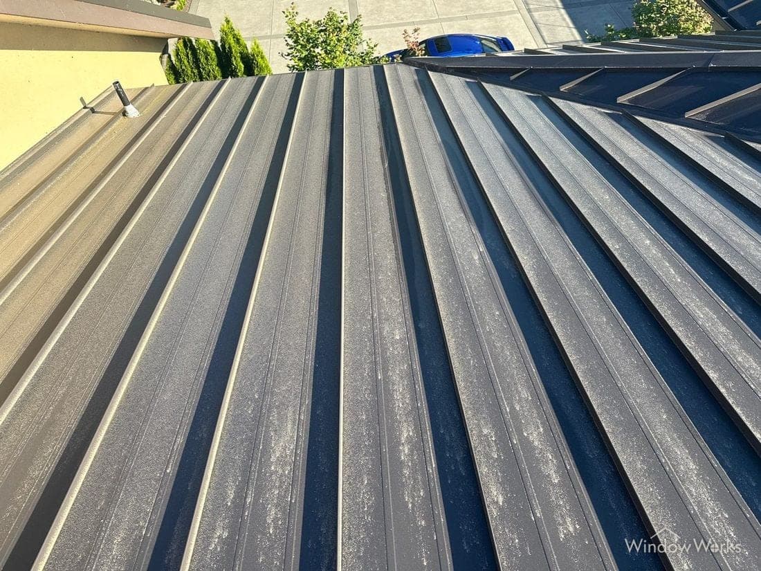 A dark standing seam metal roof covered in a pale yellow-green haze of spring pollen.