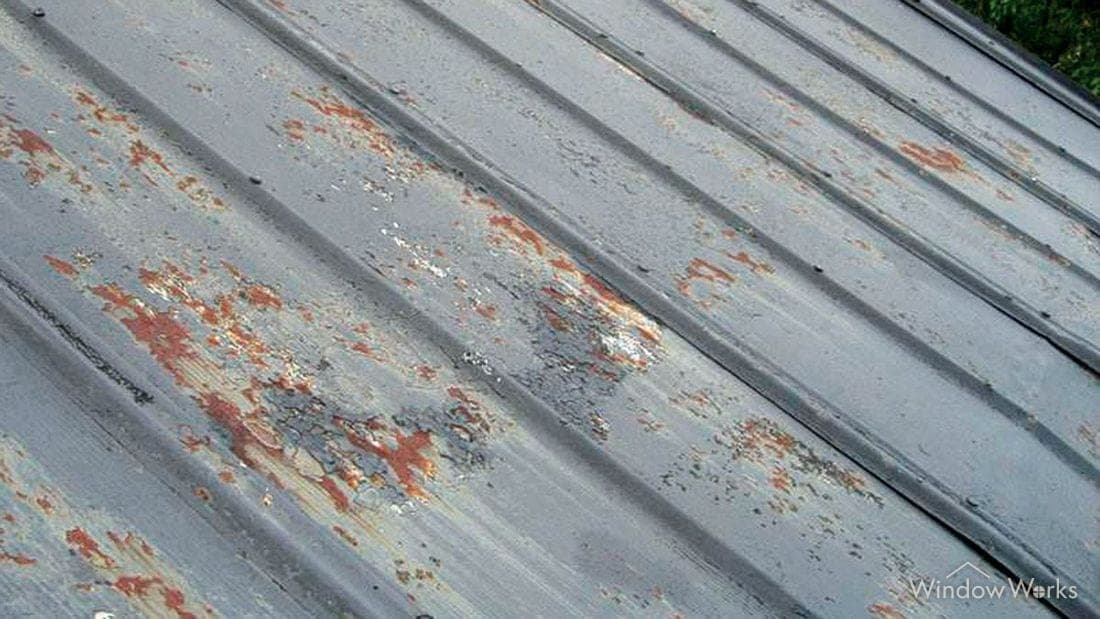 Orange surface rust breaking out along the seams and fastener lines of a metal roof panel.