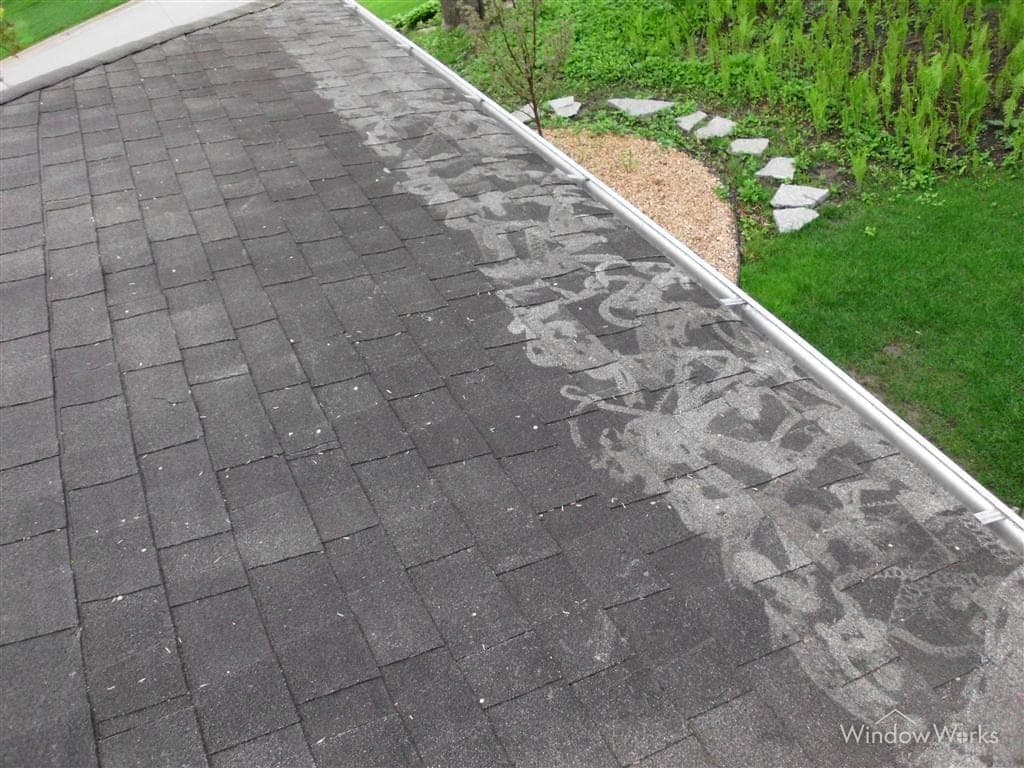 An asphalt shingle roof scarred with pale streaks where pressure washing has stripped the protective granules