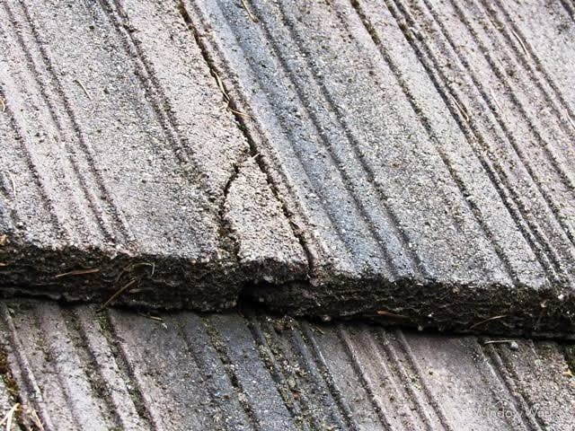 A hairline crack running across the face of a gray concrete roof tile, seen close up.