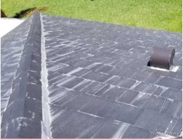 White efflorescence blooming in streaks across a dark gray flat concrete tile roof.