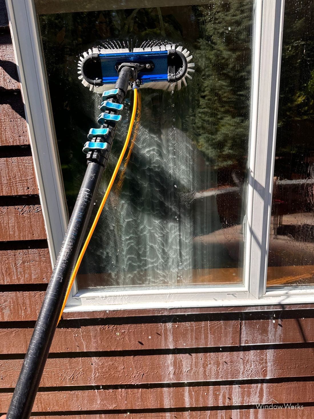 Milky white oxidation washing off a window frame and running down the glass under a water-fed brush.