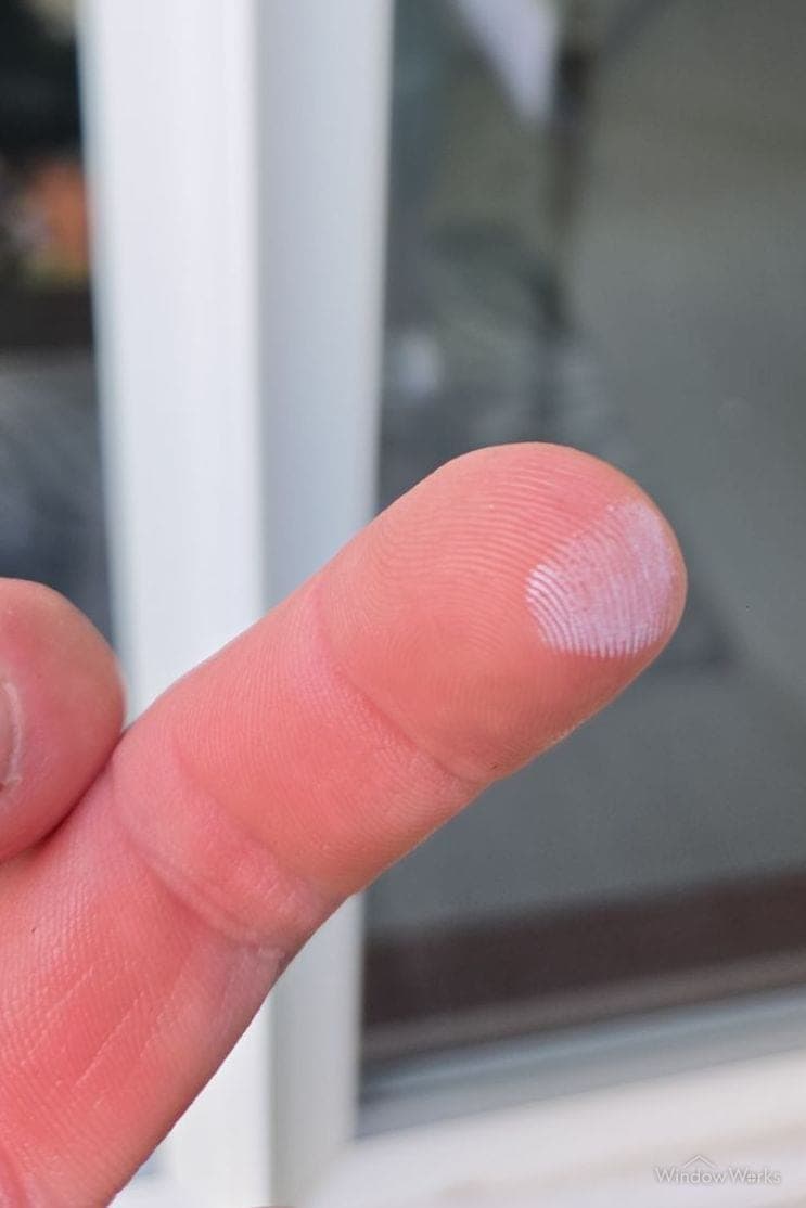 A fingertip printed with white chalk after being wiped down an oxidized window frame.