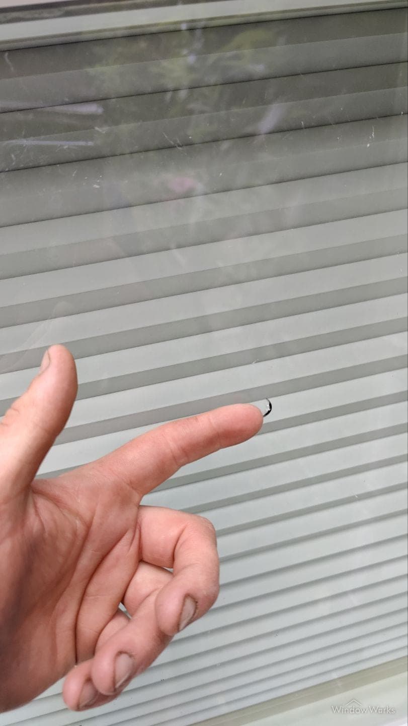 A small dark chip knocked out of the surface of a window pane.