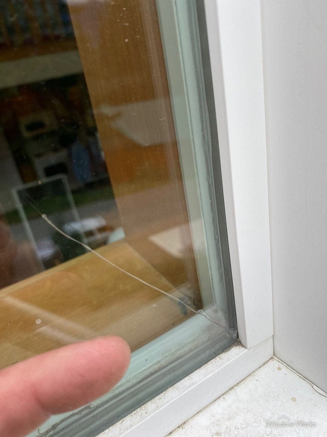 A crack running out from the edge of a window pane, with a technician's finger beside it for scale.