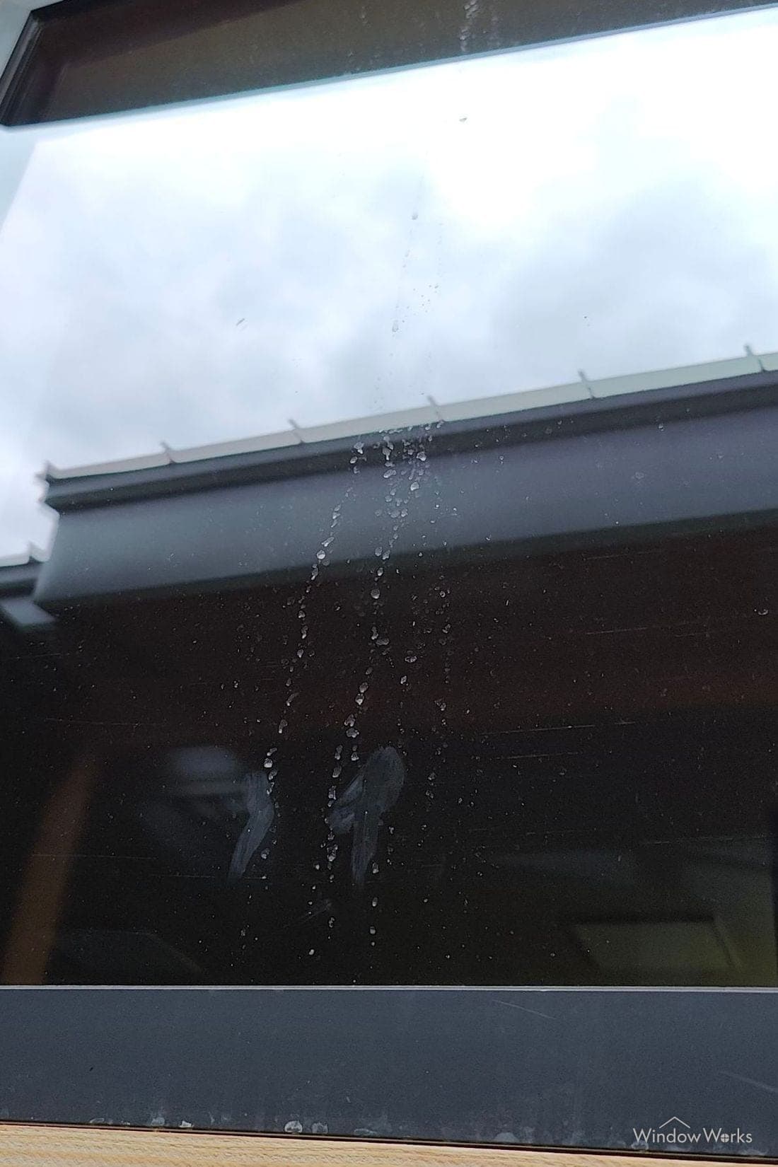 Mineral spotting running in trails down a window, showing white against the dark glass.