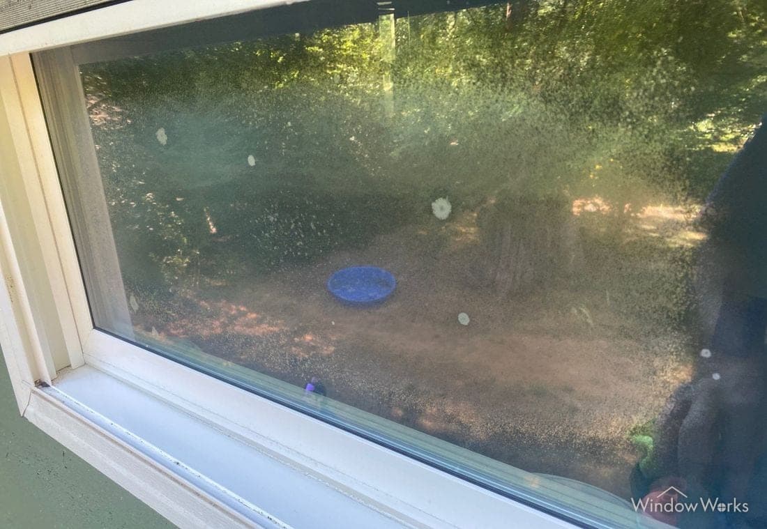 A double pane window with moisture bloom and mineral deposits sealed inside the glass.