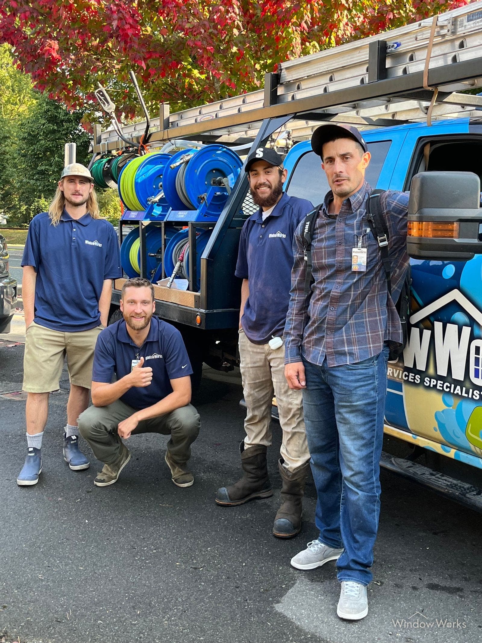 Four WindowWorks technicians beside the service truck and its hose reels under autumn maples on an Eastside job