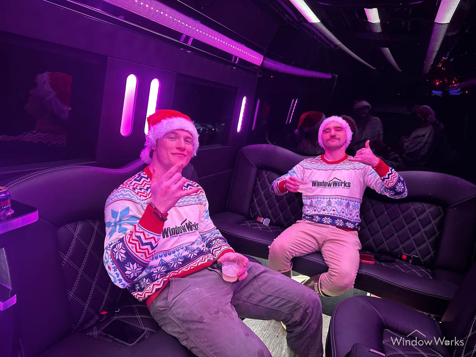 Two WindowWorks technicians in company holiday sweaters and Santa hats riding the party bus at the company holiday party