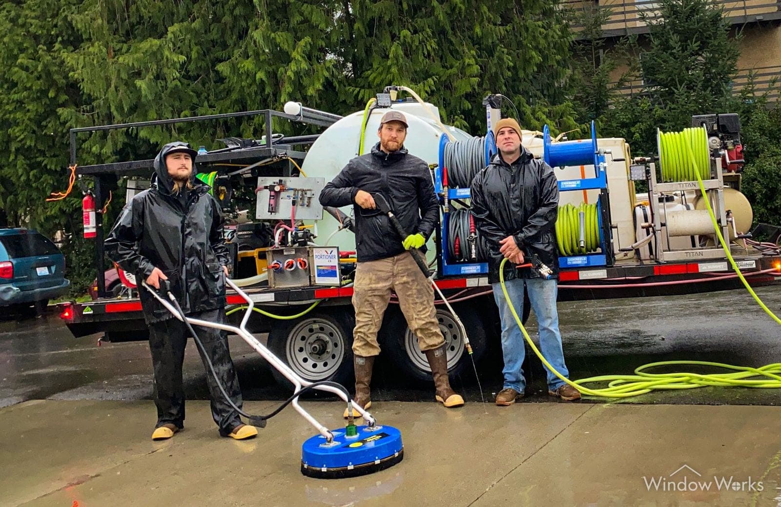 Three WindowWorks technicians in full rain gear with a surface cleaner in front of the hot-water pressure washing rig on a wet Pacific Northwest day