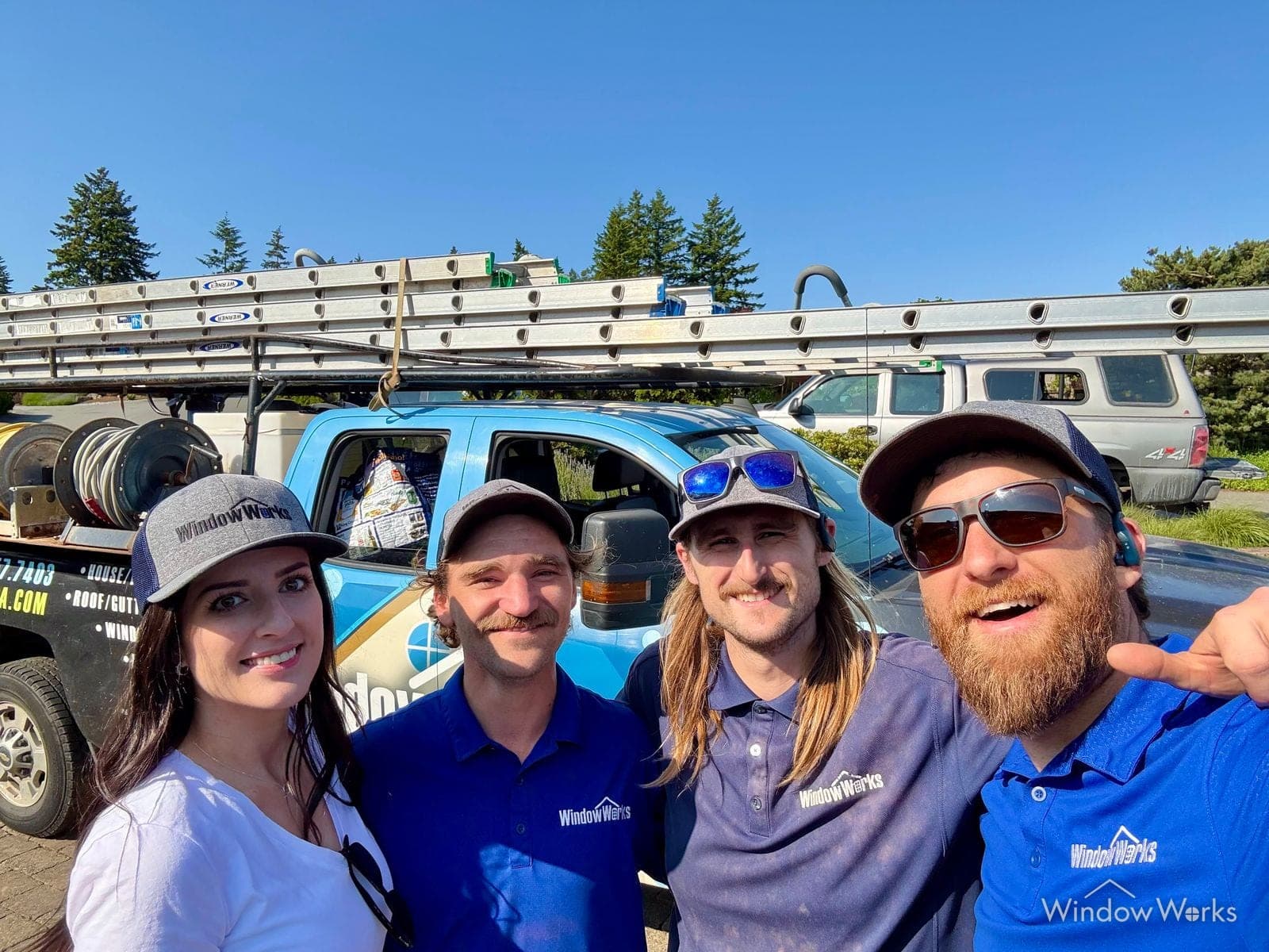 Four members of the WindowWorks team in company shirts and caps in front of the service trucks on a clear summer day