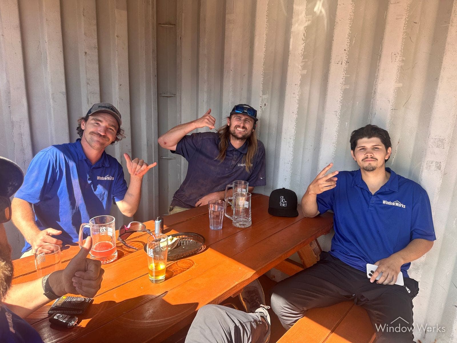 WindowWorks technicians around a picnic table at a team outing, throwing shakas and peace signs at the camera