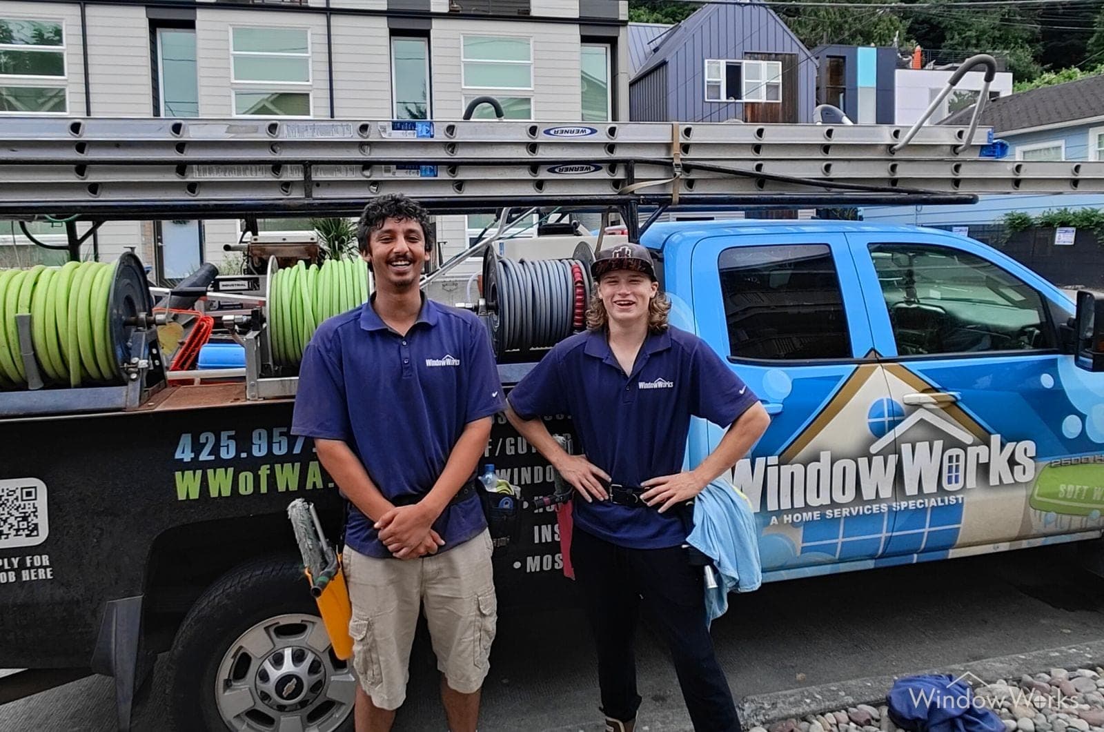 Two WindowWorks technicians in company polos in front of the loaded service truck and its hose reels on a summer evening