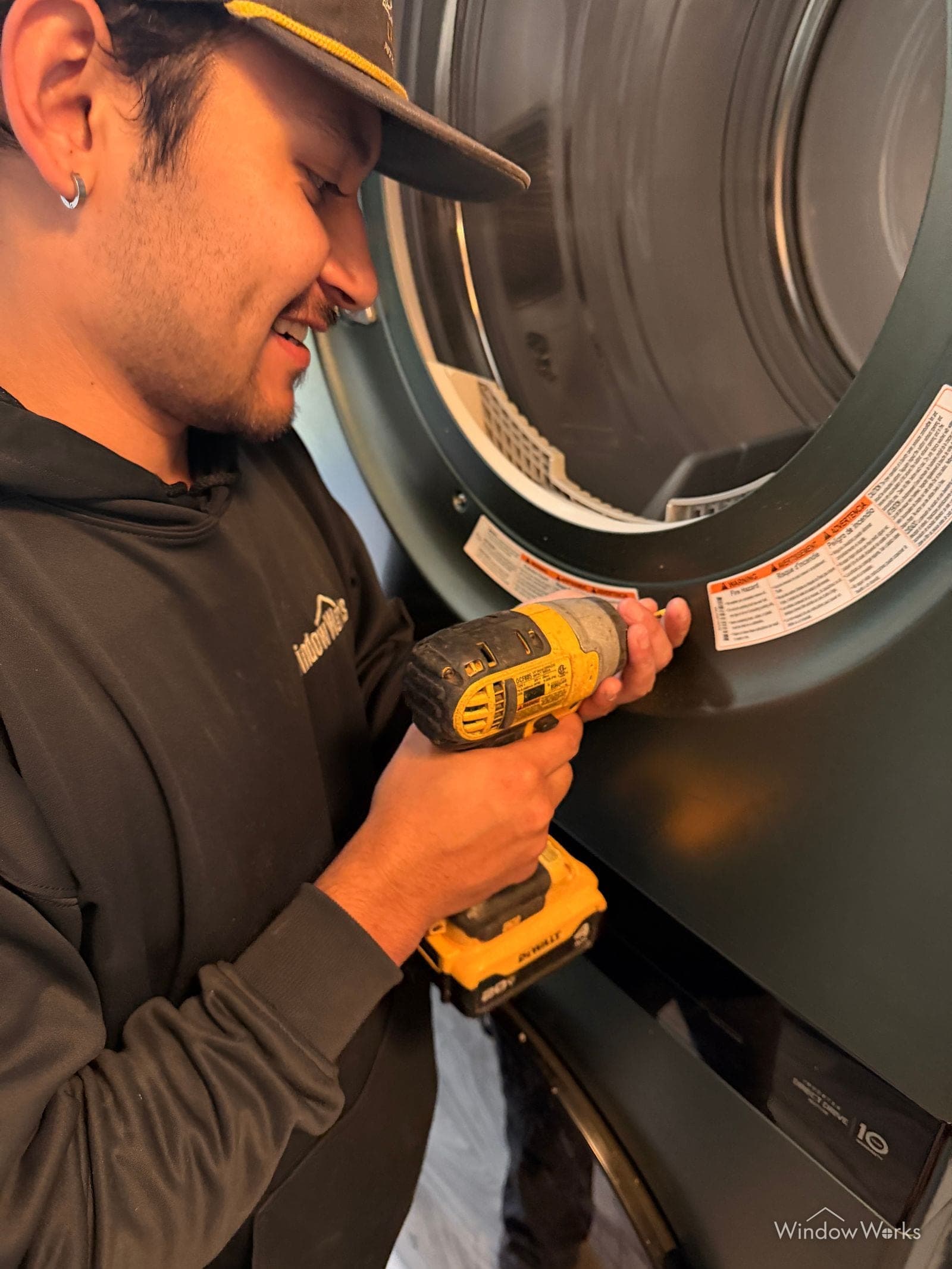 A smiling WindowWorks technician using a drill to open up a dryer for a dryer vent cleaning