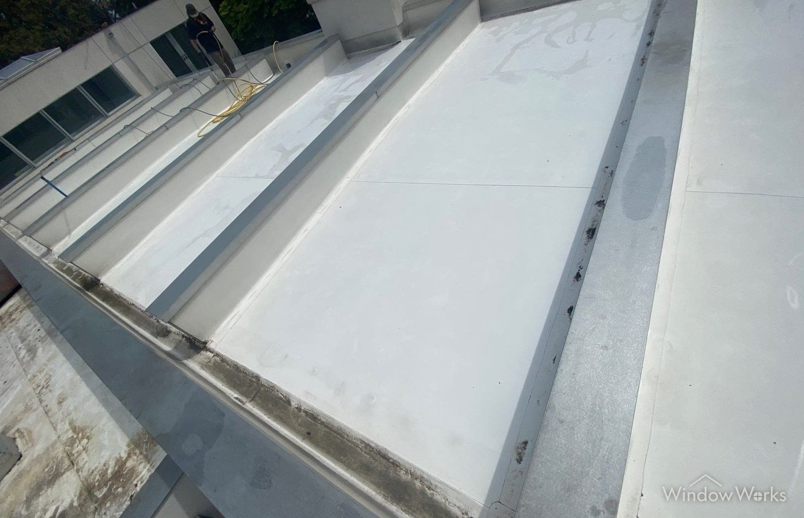 A WindowWorks technician rinsing a freshly cleaned white TPO membrane roof on an Eastside commercial building, hose lines running across the clean panels