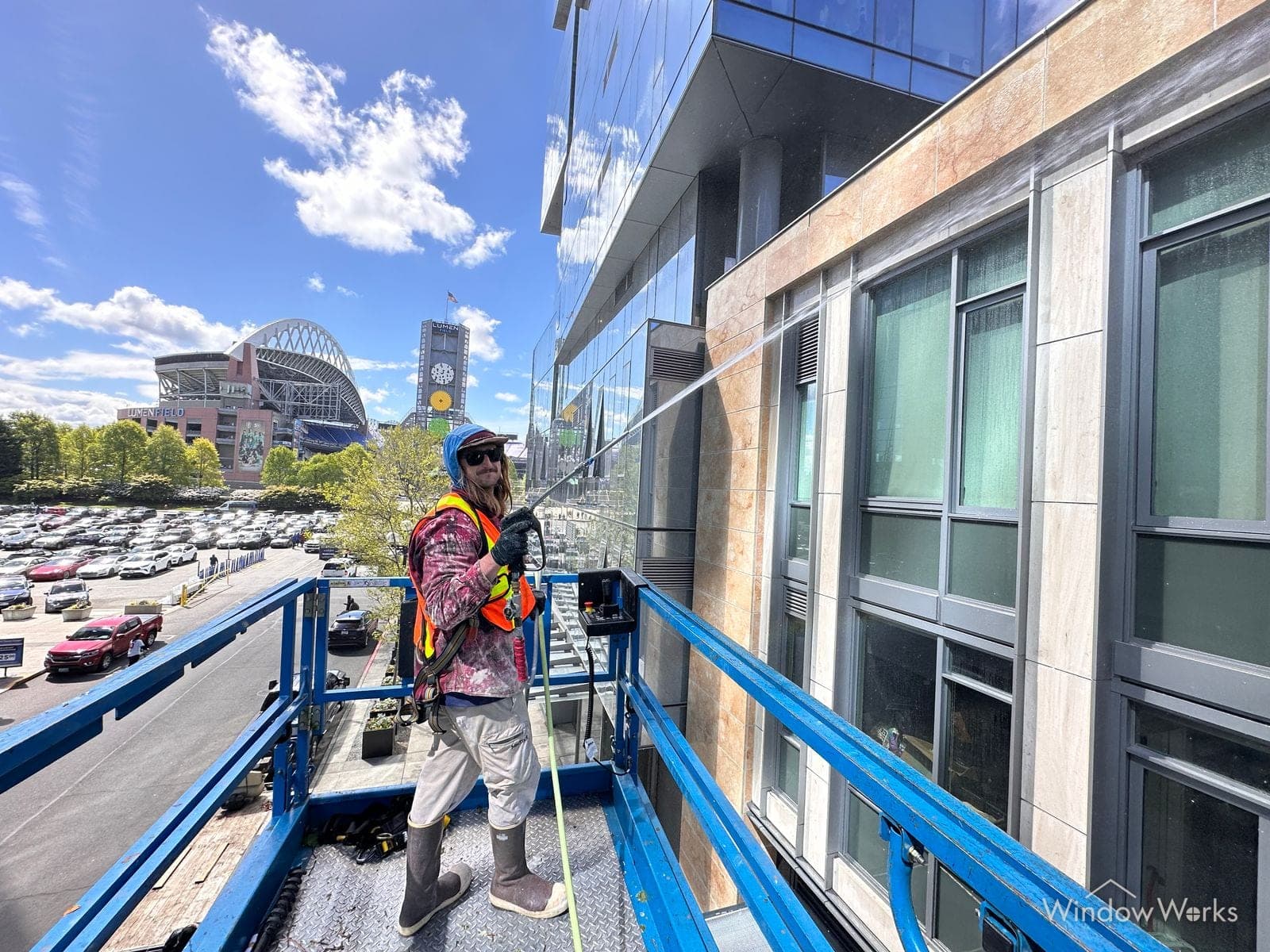 A WindowWorks technician washing a mid-rise stone facade from a lift in the stadium district