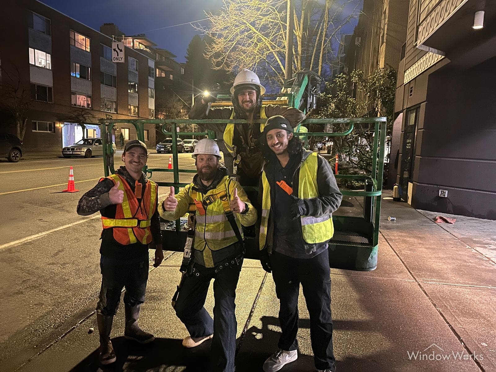 Three WindowWorks technicians in hard hats and high-visibility vests beside a boom lift on an overnight commercial job in Seattle