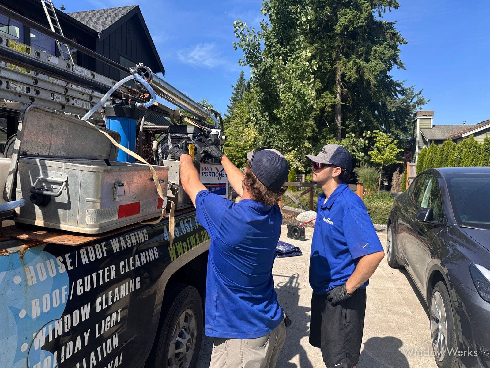 A WindowWorks technician training a teammate on the Pro Portioner soft-wash chemical dilution system at the truck