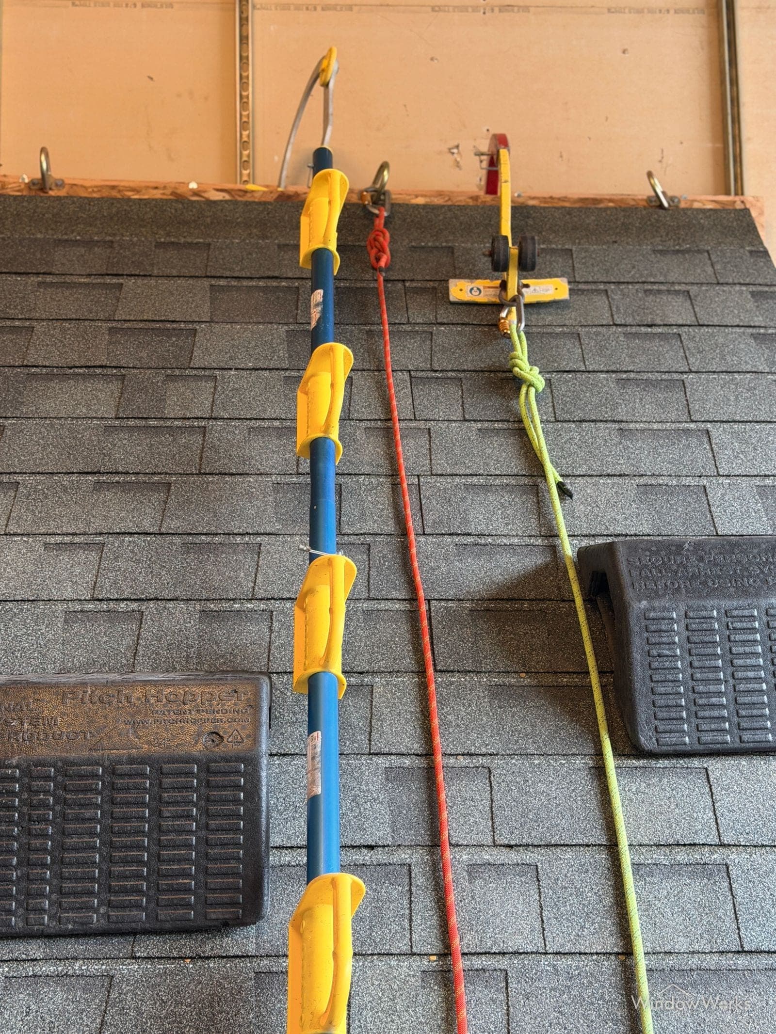 Rope, an extension pole, and roof platforms staged on the shingled mock roof inside the WindowWorks training facility