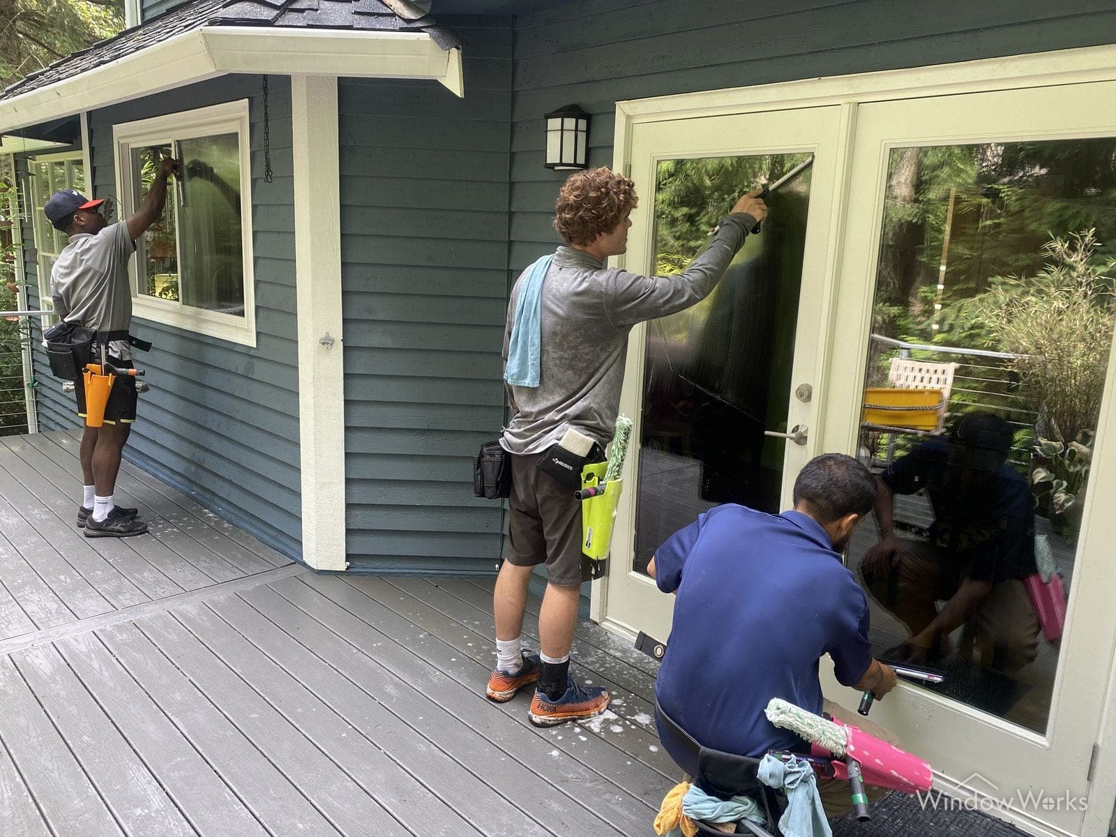 Three WindowWorks technicians cleaning the windows and French doors along the deck of an Eastside Seattle home