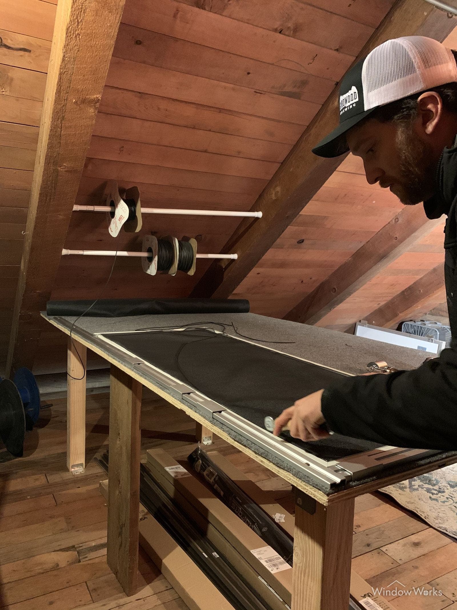 A WindowWorks technician building a replacement window screen, rolling new mesh into an aluminum frame